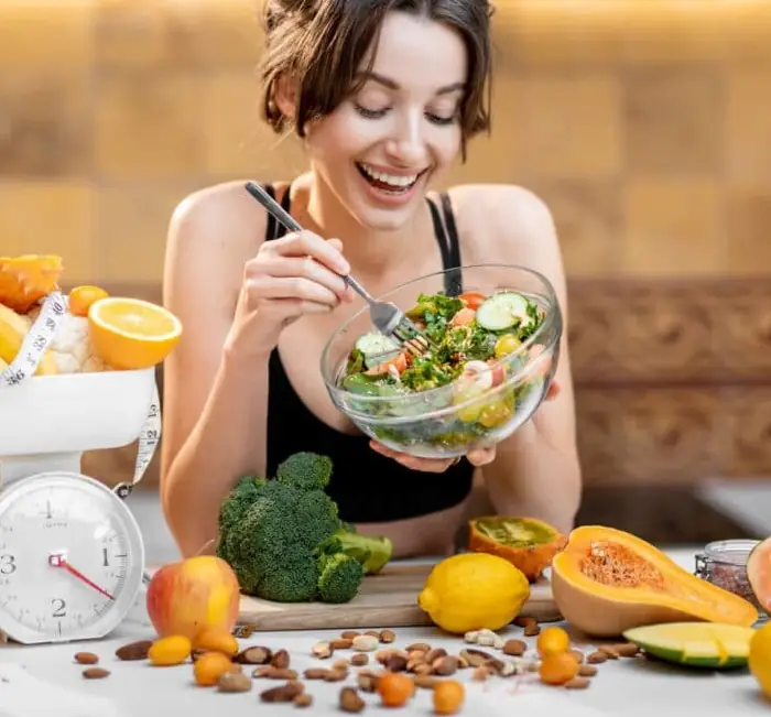 A woman eating a fresh salad surrounded by fruit and vegetables